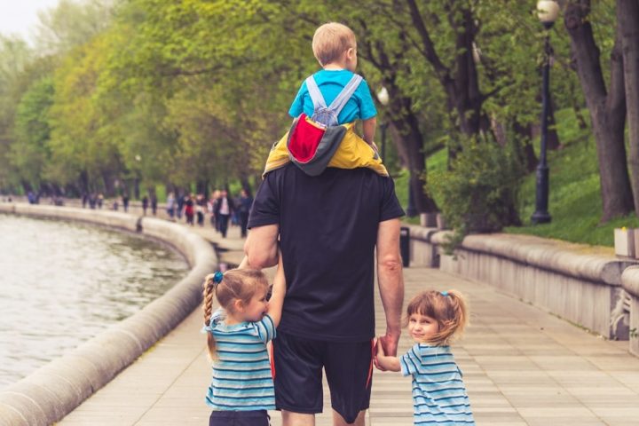 the father walks with three kids in the park